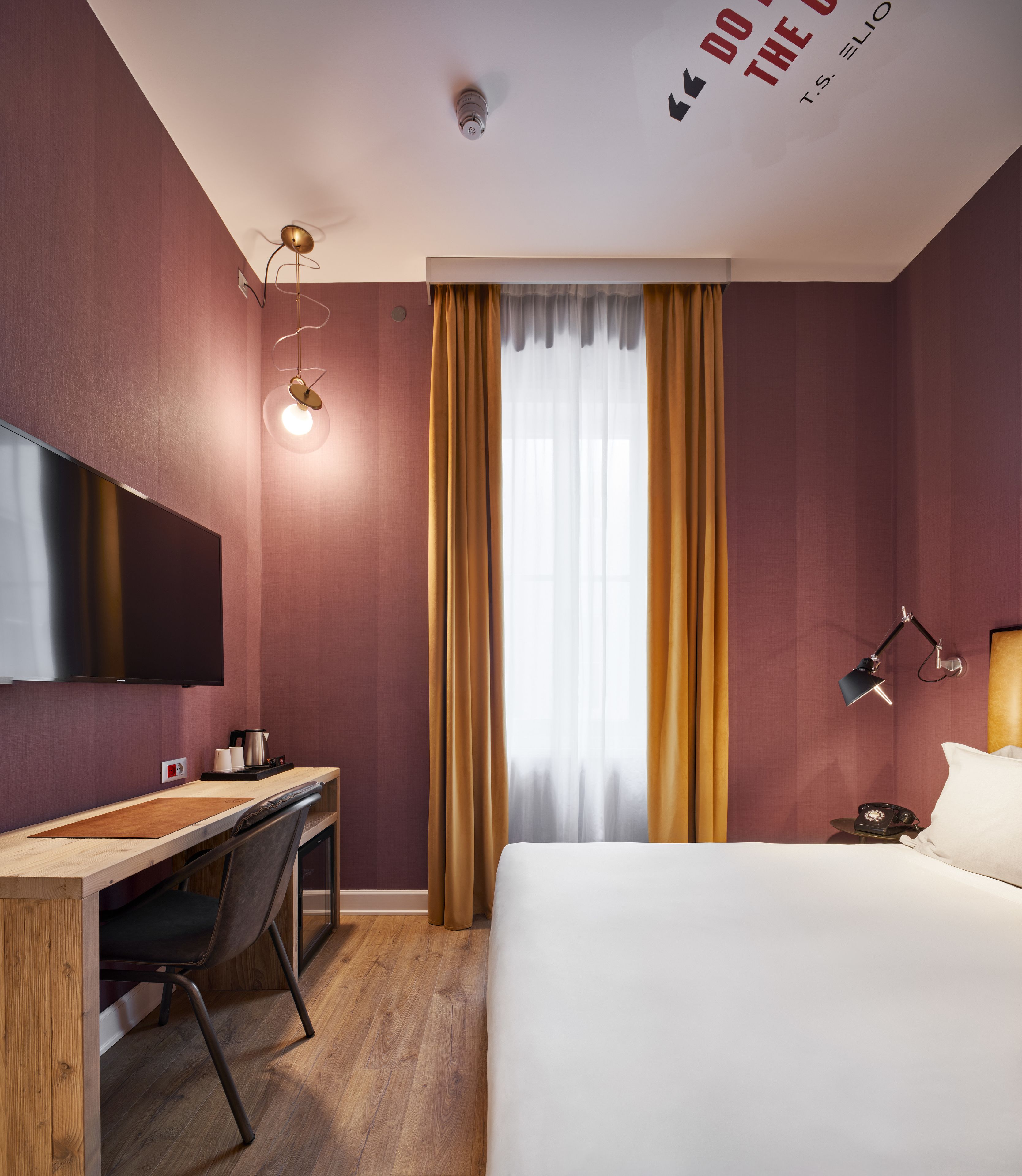 A hotel room with a bed, desk, chair, and a television on the wall.