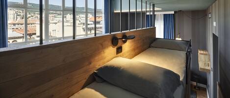 A room with a bed, a window with curtains, and a city view.