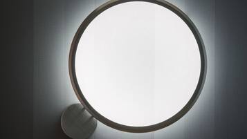 A round mirror with a light on a textured wall.