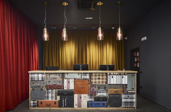A reception desk with vintage suitcases stacked on it, a red curtain, and a yellow curtain in the background.