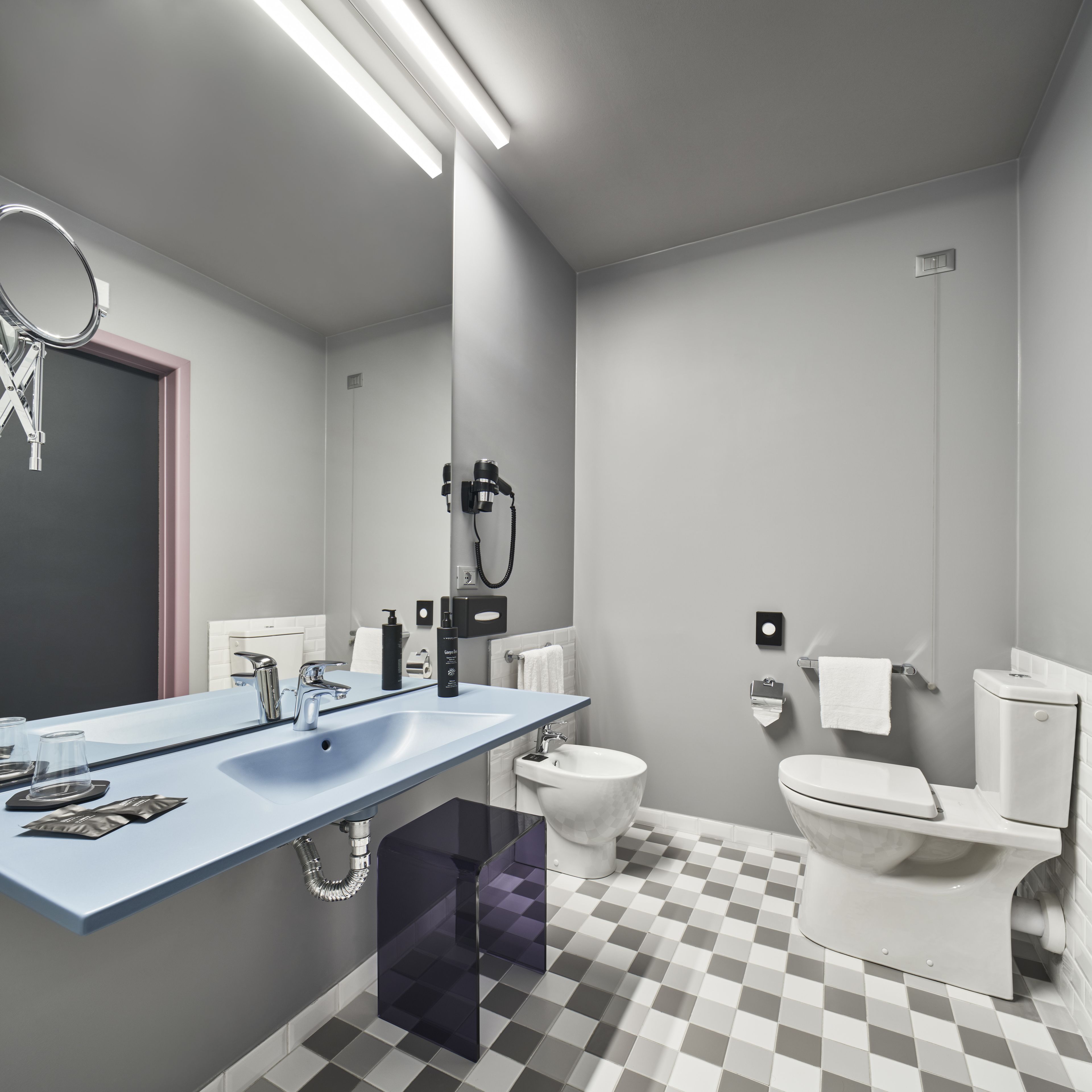 Ein modernes Badezimmer mit einem blauen Waschtisch, weißen Sanitärobjekten und einem Schachbrettfußboden.