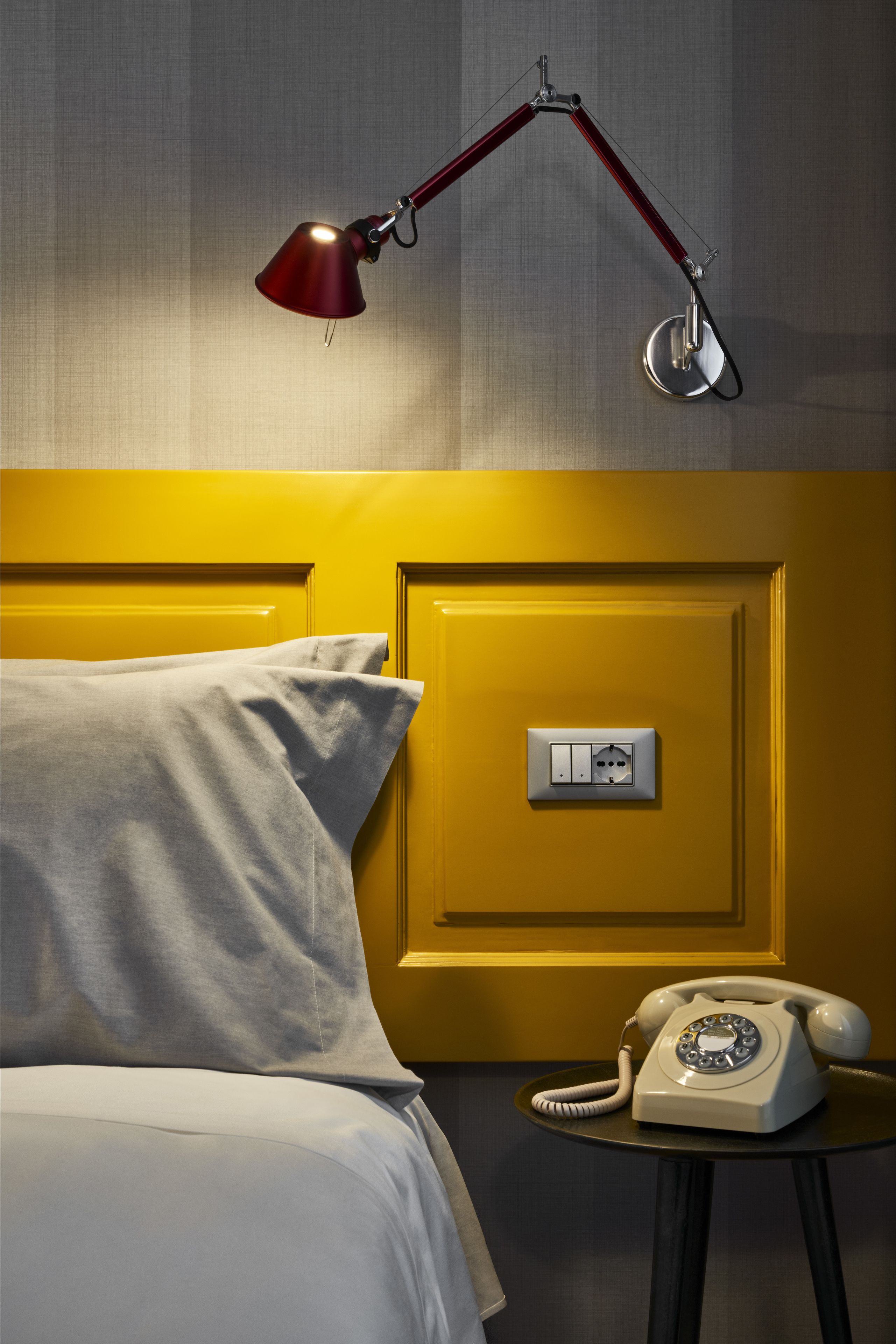 Una habitación de hotel con una cama, una mesita de noche con teléfono y una lámpara de escritorio.