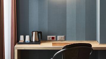 A modern room with a round mirror, a wooden desk, a black chair, and a coffee maker.