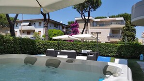 A hot tub area with outdoor seating and umbrellas, surrounded by hedges and buildings in the background. - Hotel Marebello (Tortoreto)