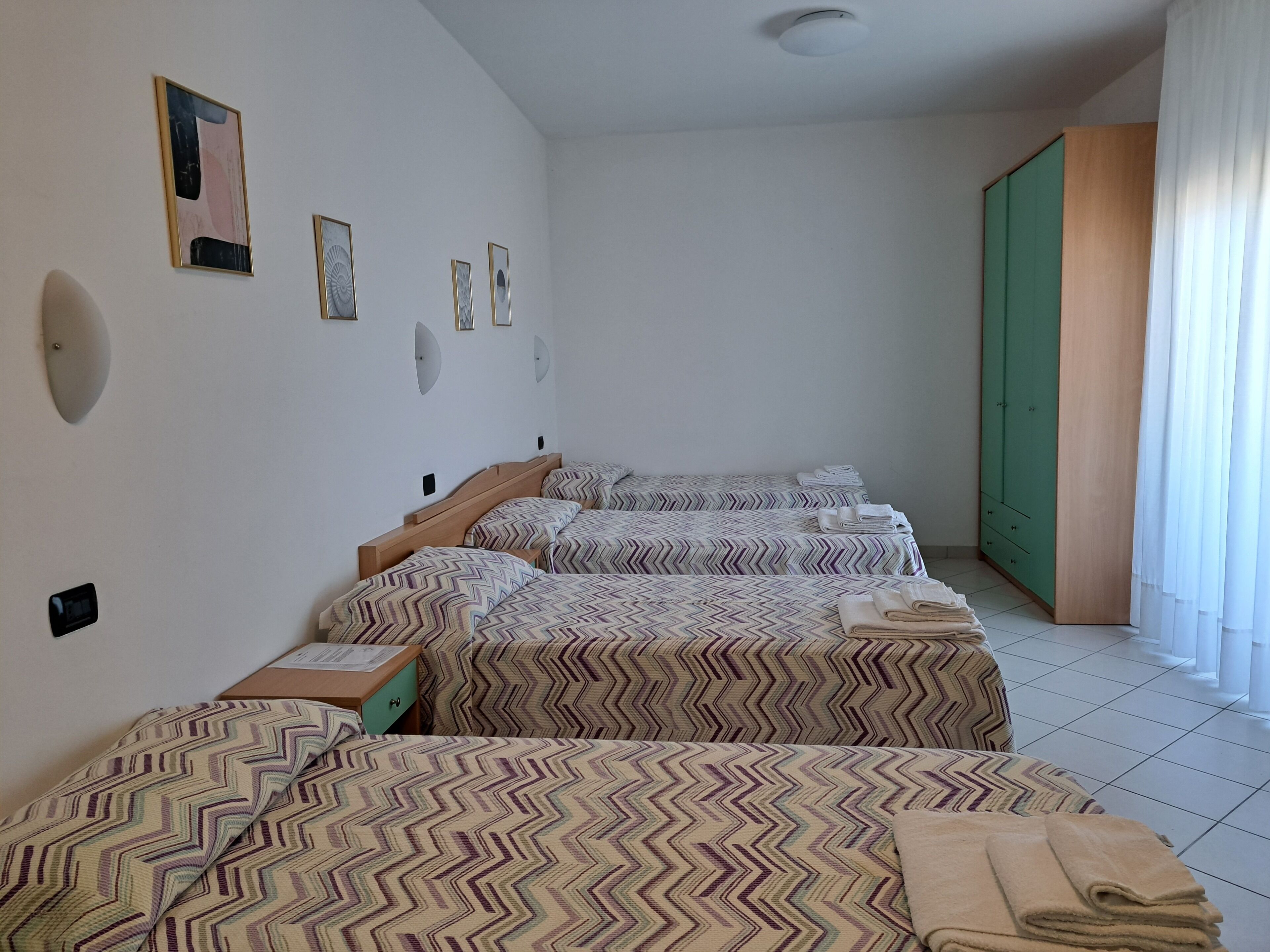 Habitación de hotel con tres camas, un armario de madera y una puerta verde.