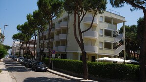 Un edificio a più piani con balconi, auto parcheggiate e alberi.