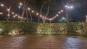 Area esterna pavimentata con luci a tendina e alberi.