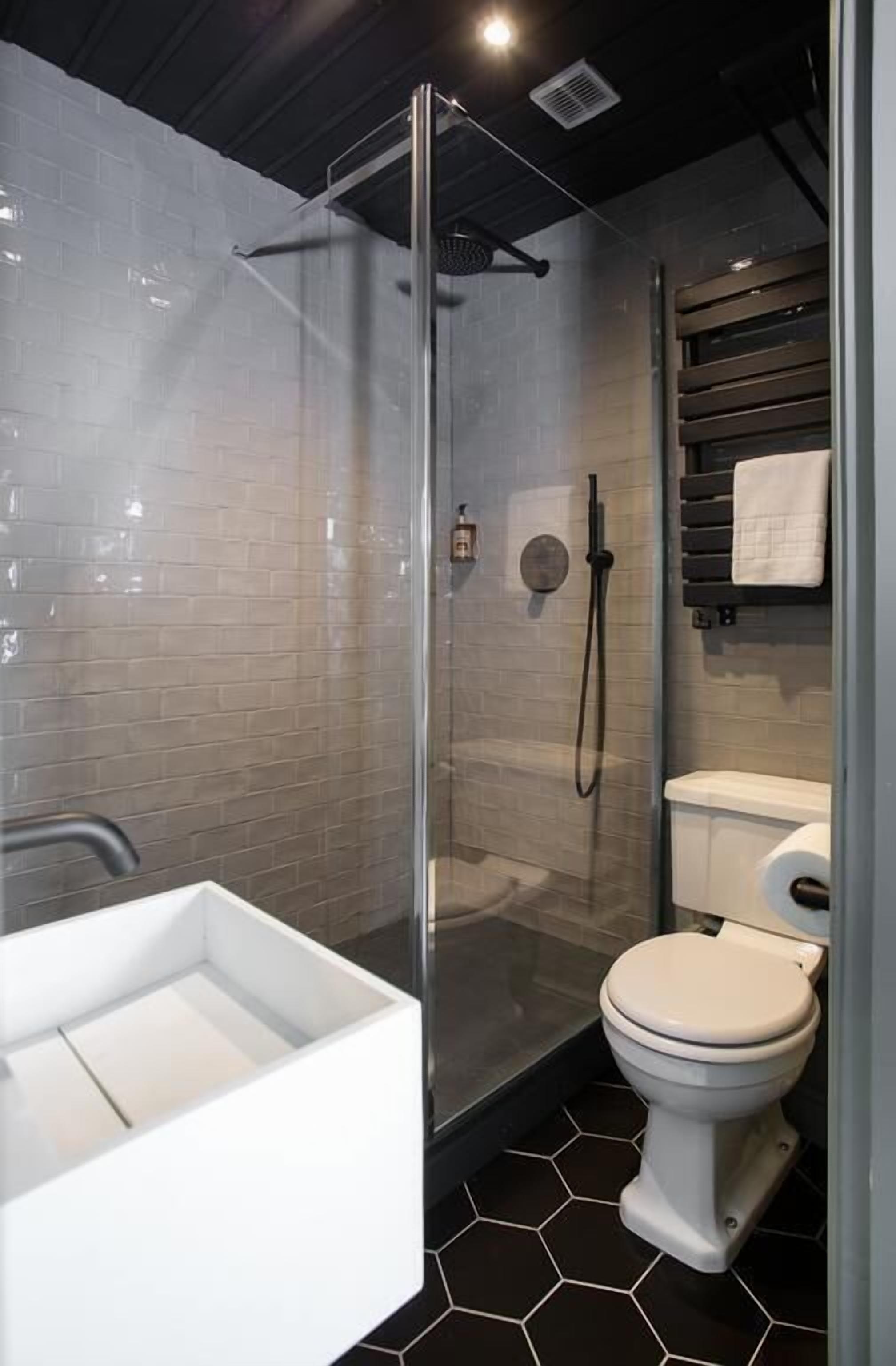 Un baño moderno con ducha de vidrio, inodoro y lavamanos blancos.