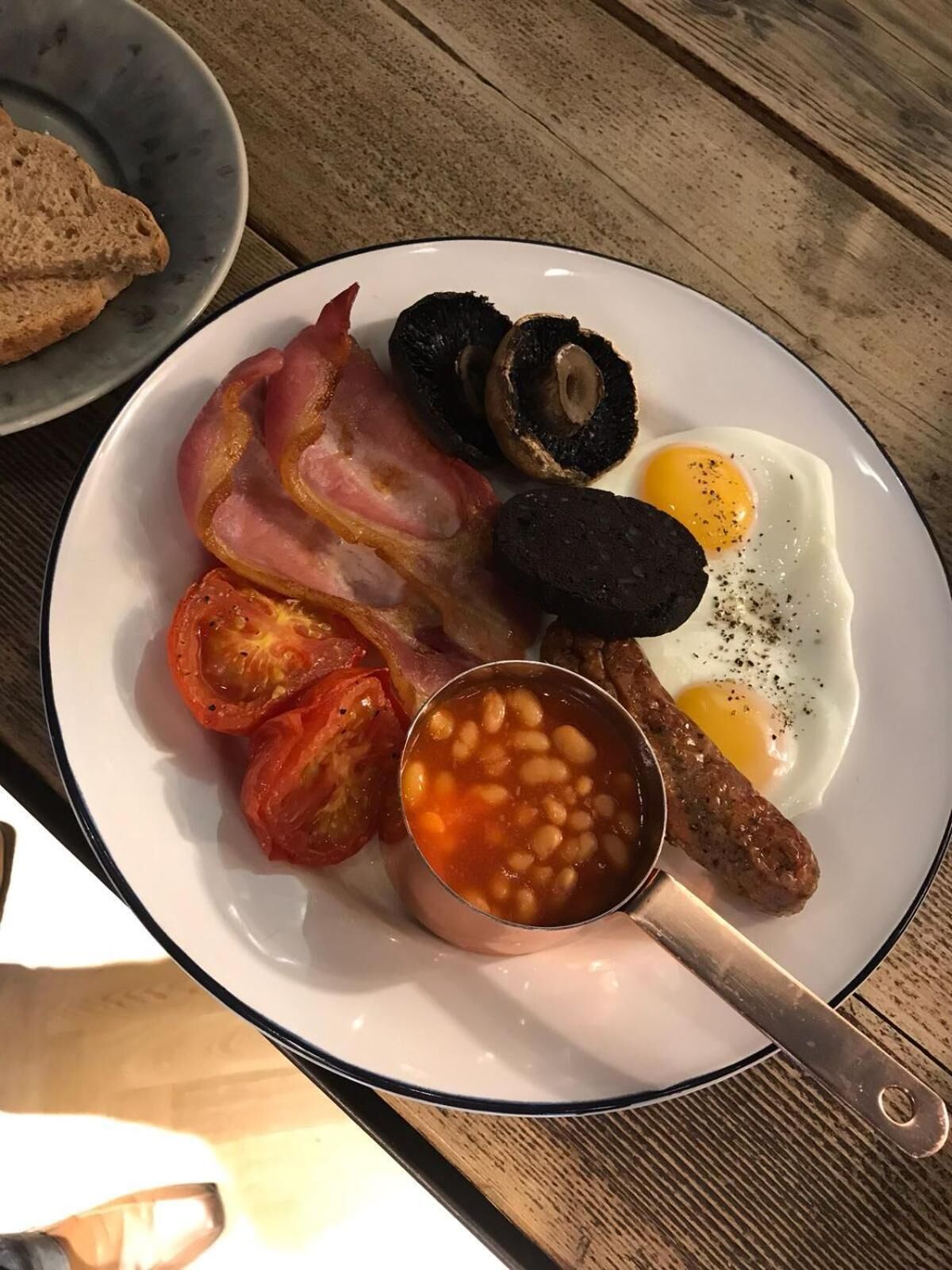 A plate with bacon, eggs, mushrooms, sausages, and beans.