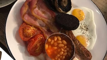 A plate with bacon, eggs, mushrooms, sausages, and beans.