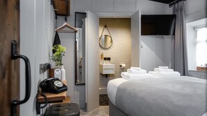 A modern hotel room with a bed, a bedside table with a telephone, a hanging mirror, a sink with toiletries, and a TV mounted on the wall. - The Pickled Parson of Sedgefield (Stockton-on-Tees)