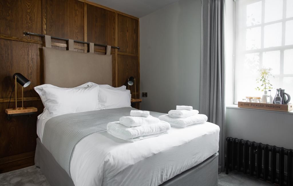 Een net opgemaakt bed met witte lakens en opgevouwen handdoeken, een houten hoofdbord, nachtlampjes en een raam met uitzicht.