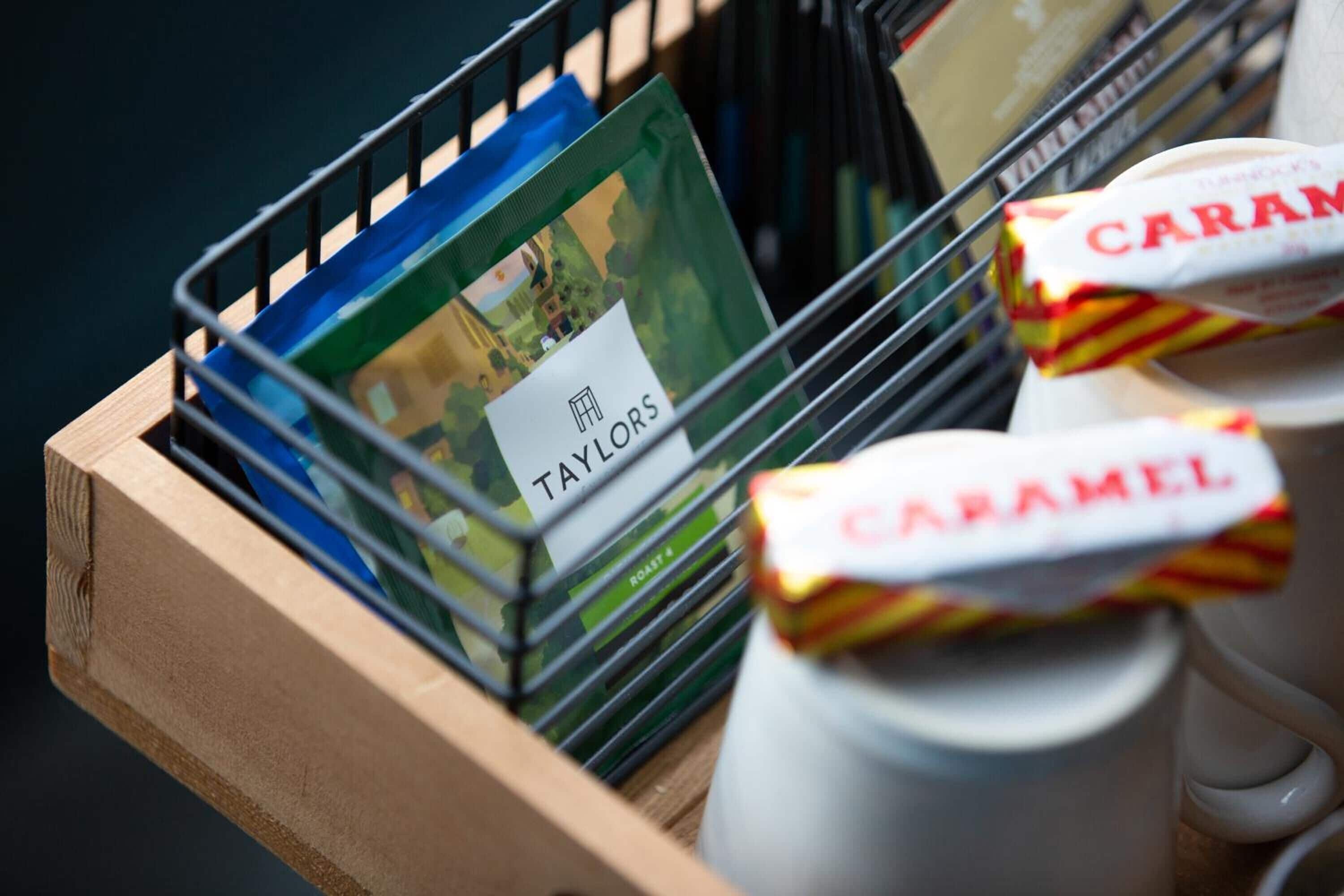 A wooden tray with a stack of magazines, a coffee cup, and a box of caramel-flavored treats.