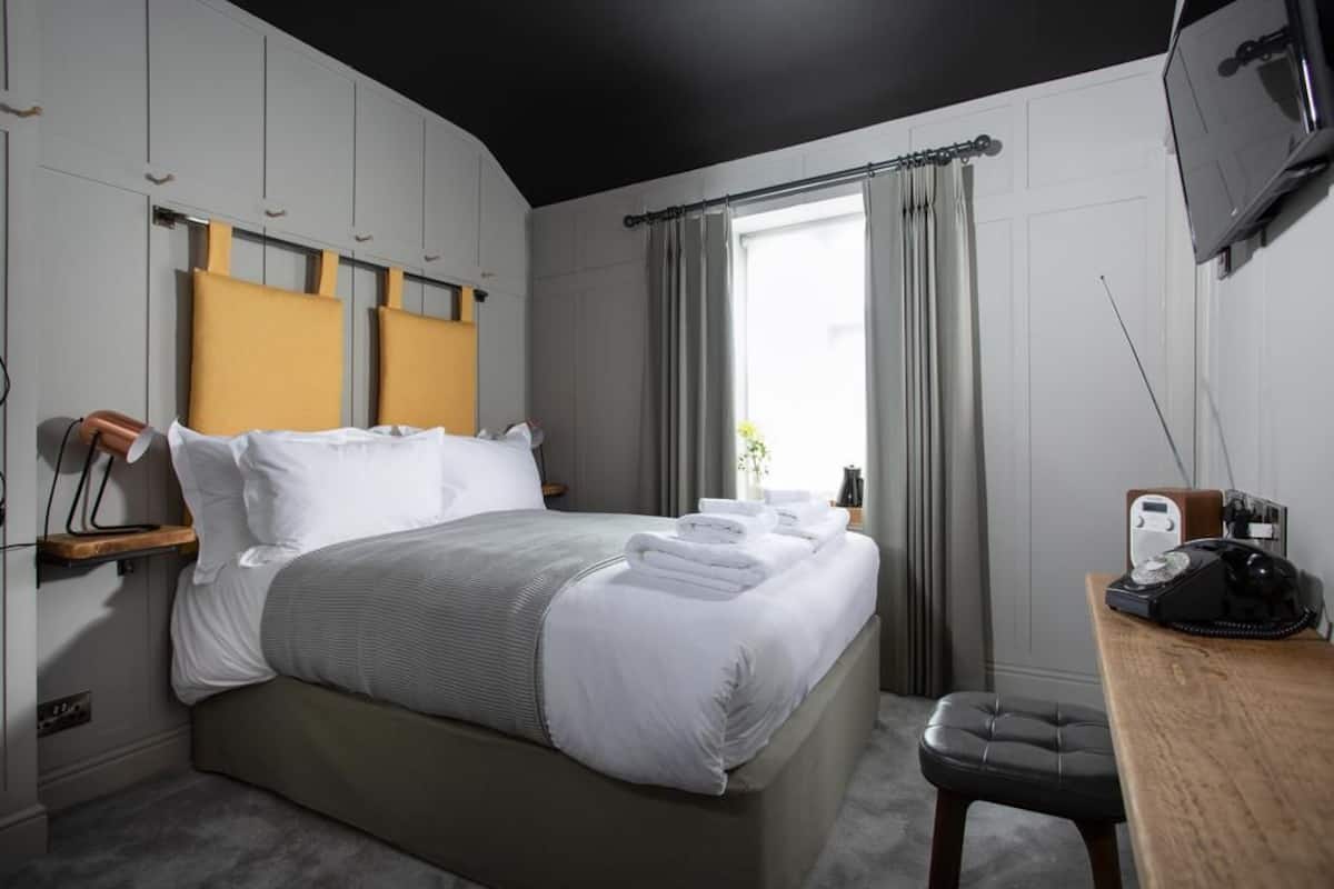 A modern hotel room with a bed, a desk, a telephone, and a television.