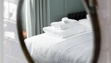 A room with a bed, white towels, a mirror, and a window with curtains.