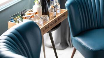 Ein Holztablett mit Flaschen und Gläsern auf einem Tisch, platziert zwischen zwei blauen Stühlen.