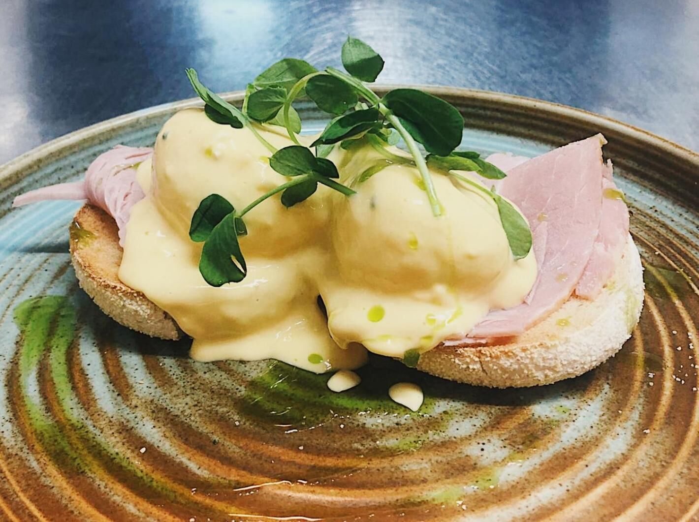 A plate with a sandwich, hollandaise sauce, and greens.