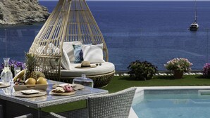 A wicker lounge chair with cushions, a dining table with fruits and a glass, and a pool with a view of the sea and a yacht. - Felini Palace (Malevizi)