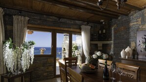 A rustic dining area with a stone wall, wooden ceiling, and a view of the sea. - Felini Palace (Malevizi)