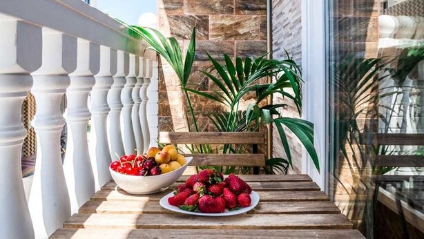 A wooden table with a bowl of fruit and a plate of strawberries on a balcony. - Hostal Poseidón (San Bartolomé de Tirajana)