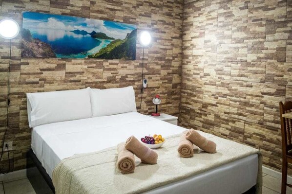 Una cama bien hecha con sábanas blancas, dos toallas enrolladas y un frutero sobre la cama.