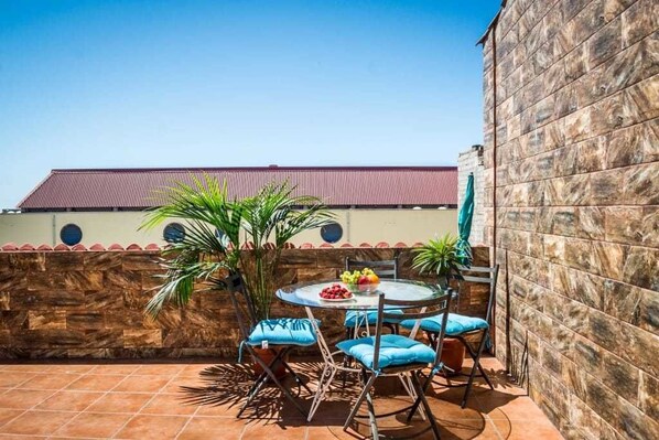 Un patio con una mesa redonda y sillas, rodeado de muros de piedra y un suelo de baldosas.