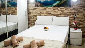 A hotel room with a bed, a bedside table with a lamp, a wall with a painting, and a mirror. - Hostal Poseidón (San Bartolomé de Tirajana)