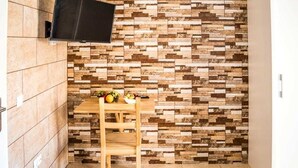A small room with a tiled floor, a wooden table with fruits, and a wall-mounted TV. - Hostal Poseidón (San Bartolomé de Tirajana)