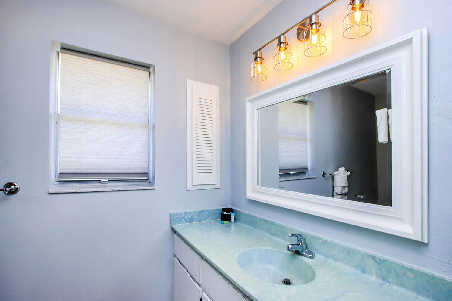 Une salle de bain avec un grand miroir, un lavabo et une fenêtre avec des stores.