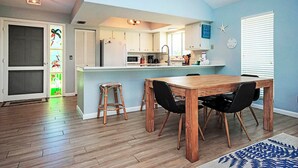 A modern kitchen with a central island, wooden dining table, and black chairs. - On a Whim Captiva Island Beach Cottage (Captiva)