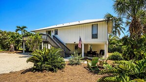 A two-story house with a covered patio area, a flag, and tropical landscaping. - On a Whim Captiva Island Beach Cottage (Captiva)