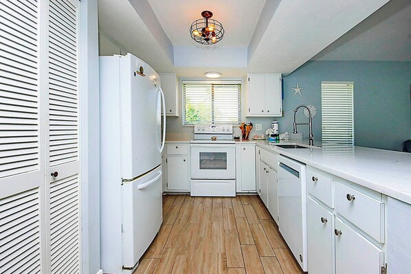 A compact kitchen with white cabinetry, a built-in oven, a refrigerator, and a window with blinds.