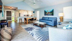 A spacious living area with a sofa, coffee table, and a dining table. There is a kitchen in the background with a ceiling fan. - On a Whim Captiva Island Beach Cottage (Captiva)