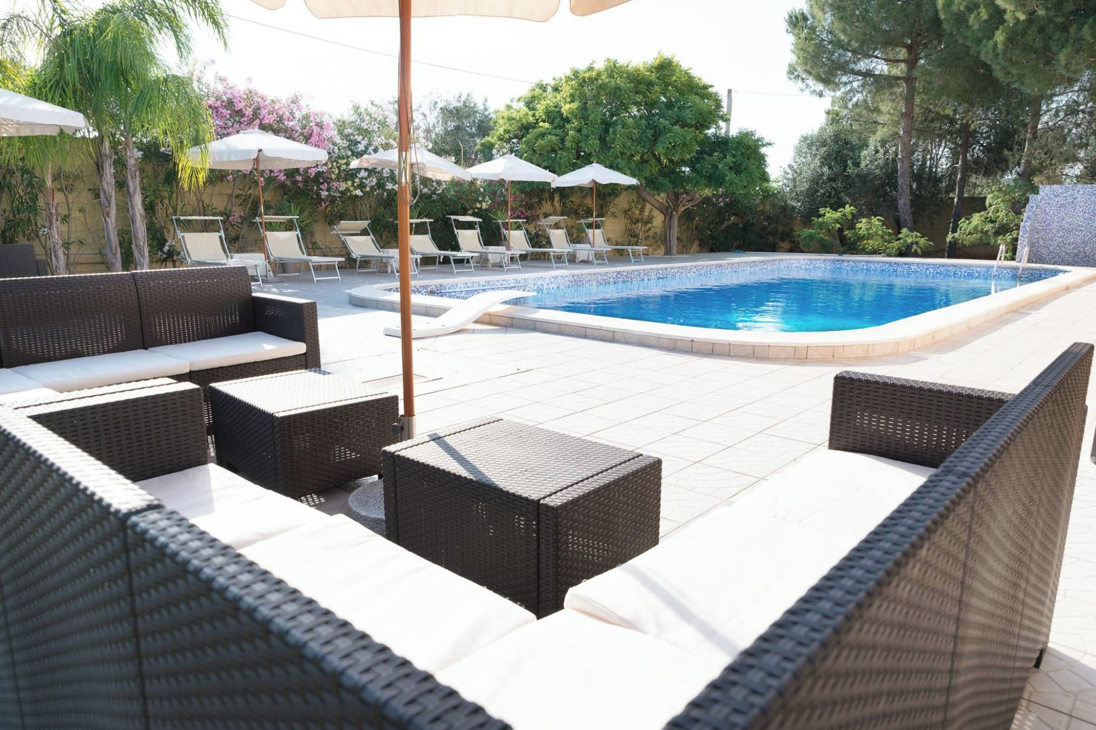 A poolside area with wicker furniture, umbrellas, and a tiled deck.