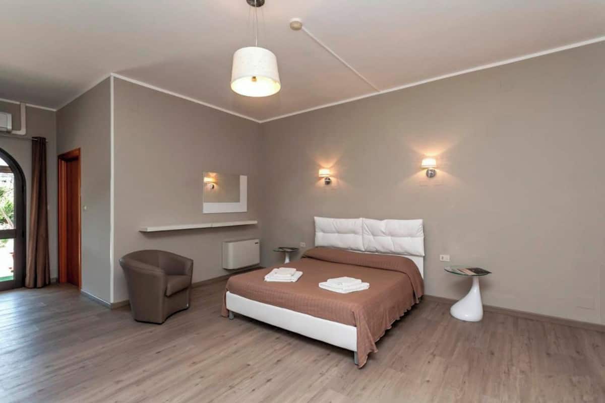 Ein modernes Schlafzimmer mit einem großen Bett, Nachttischen, einem Sessel und einer Pendelleuchte.