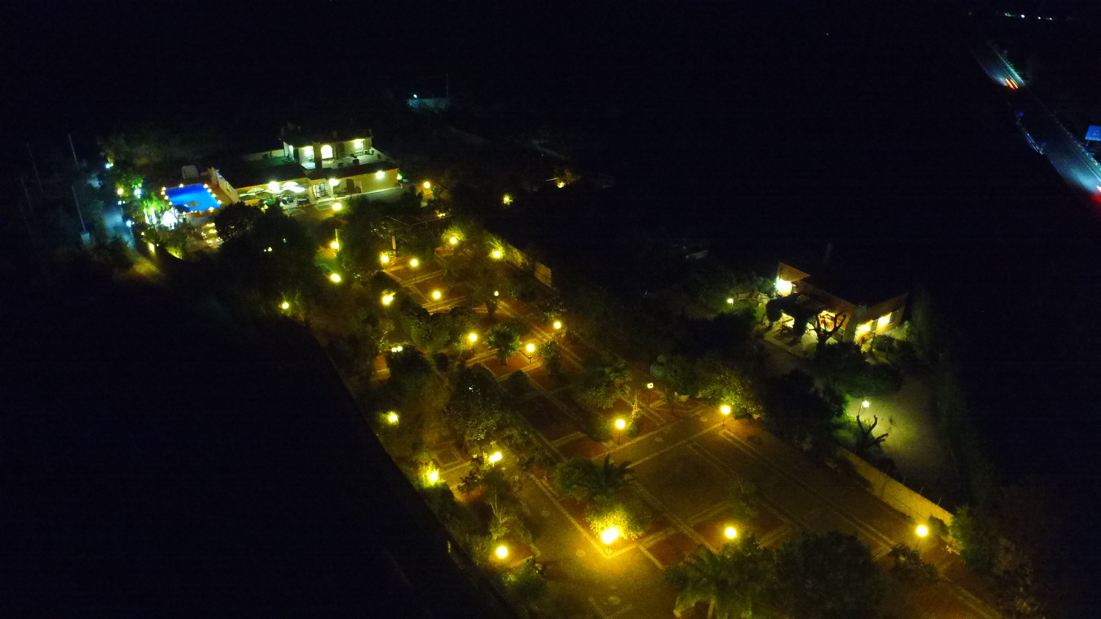 An aerial view of a well-lit area with multiple buildings, roads, and greenery.