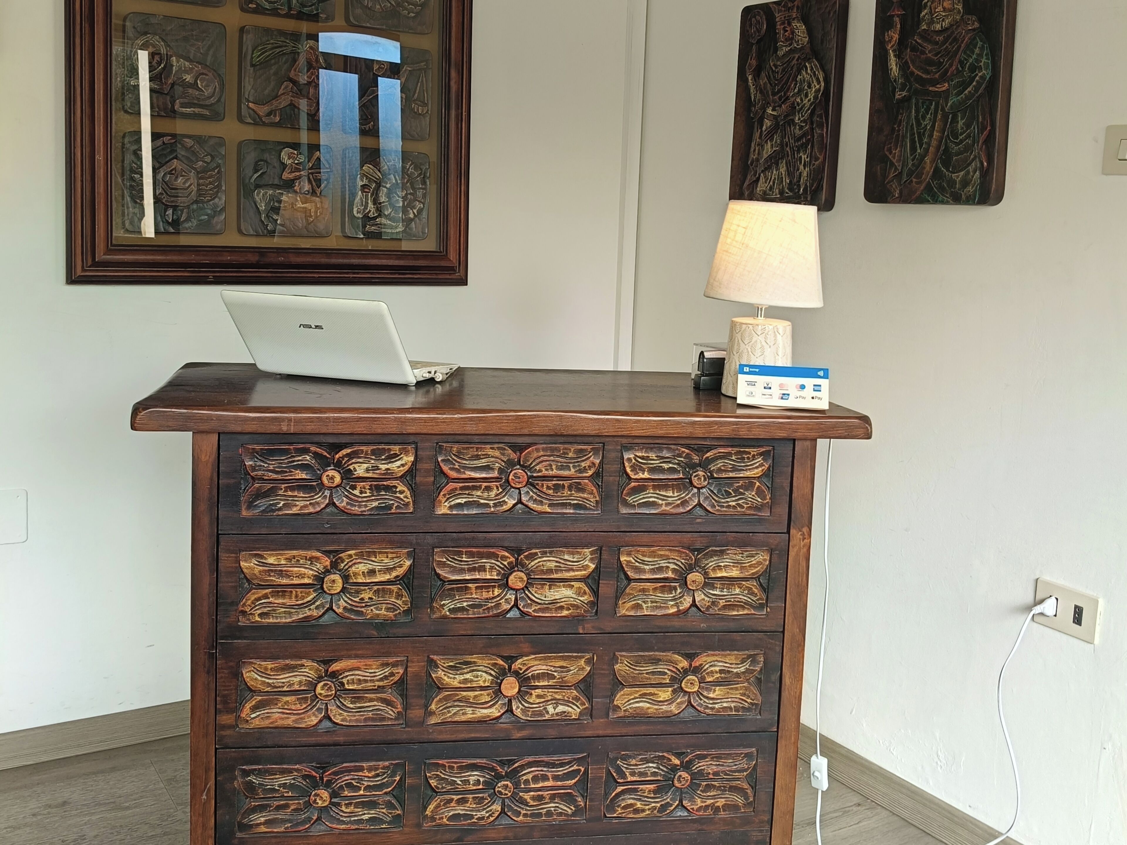 A wooden cabinet with a laptop on top, a lamp, and a wall-mounted artwork.