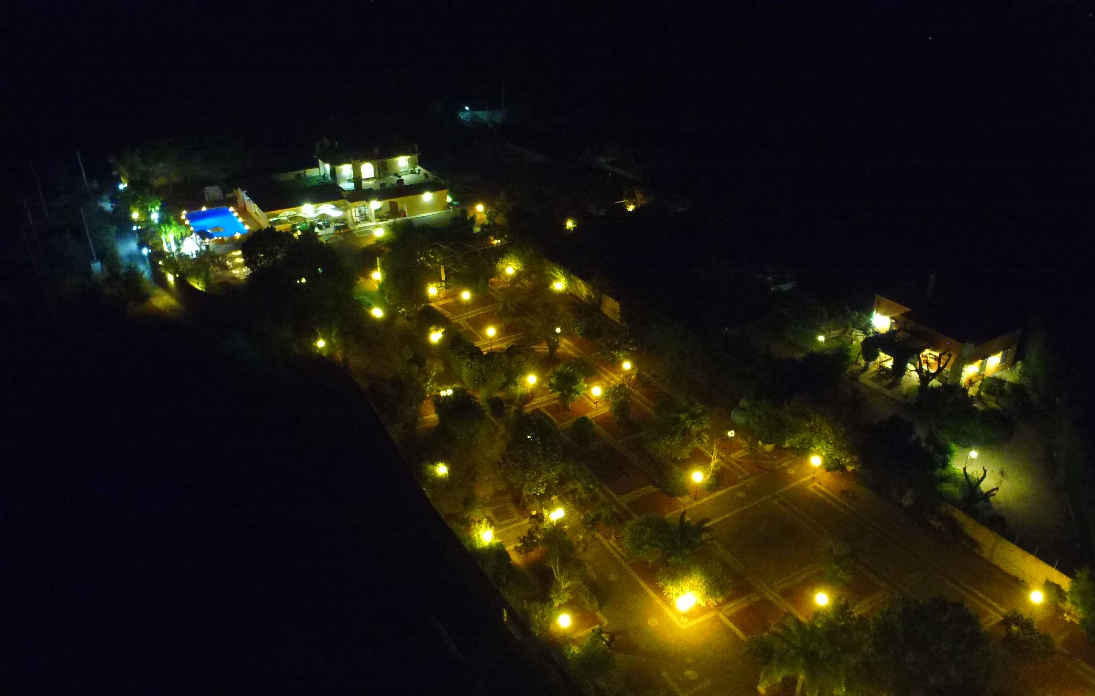 An aerial view of a hotel with a swimming pool, multiple illuminated areas, and a parking lot.