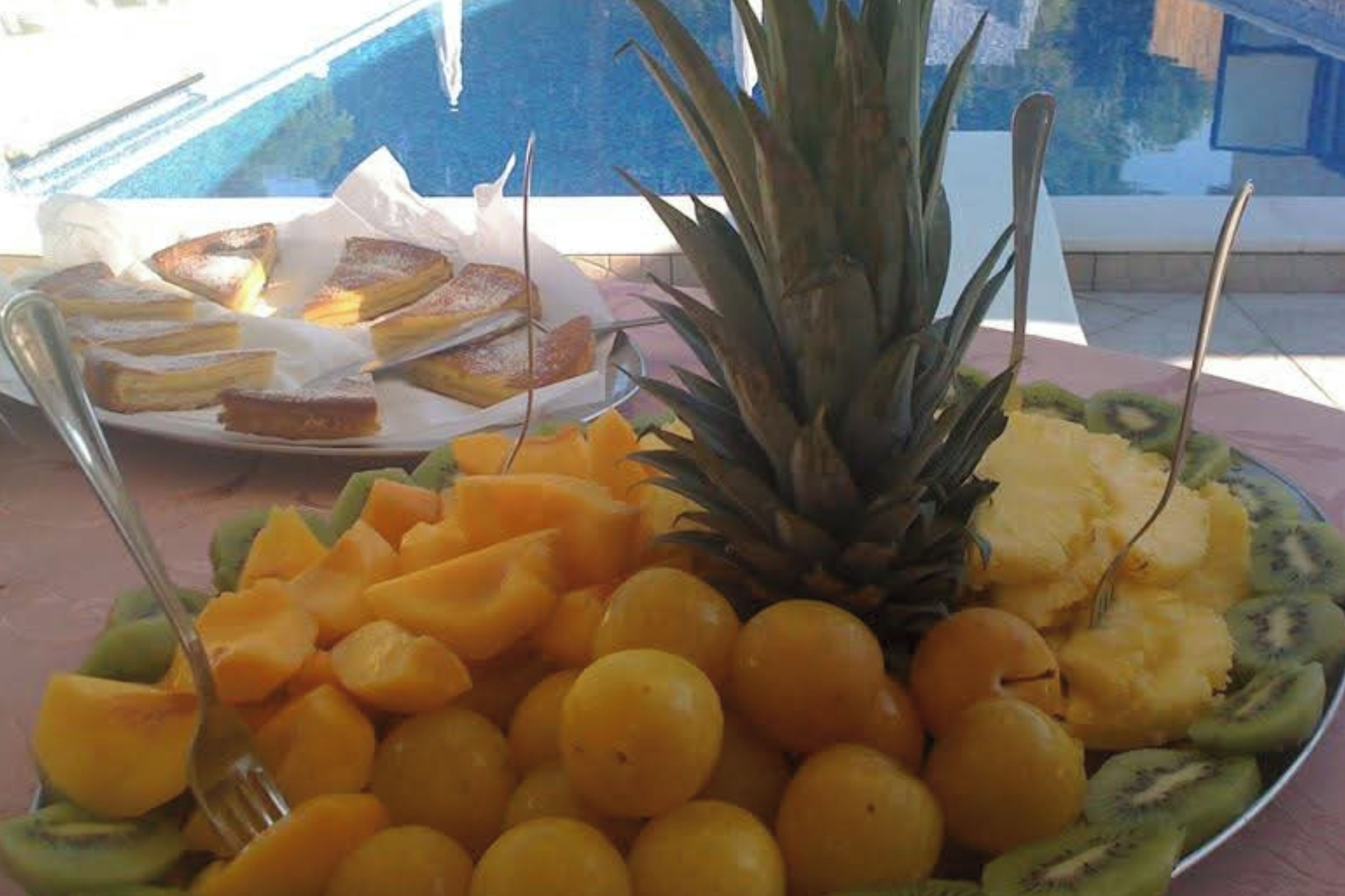 Uma travessa de frutas com abacaxi, kiwi e fatias de manga sobre uma mesa perto de uma piscina.