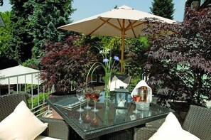 An outdoor dining area with a glass table, wicker chairs, and a large umbrella. - Der Loewen (Hagnau)