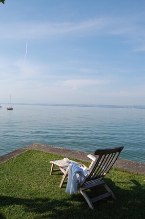 A grassy area with two wooden lounge chairs facing a calm body of water. - Der Loewen (Hagnau)