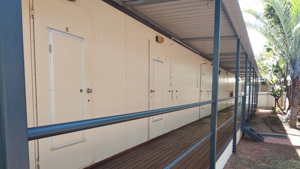 A row of white rooms with doors, a wooden deck, and a blue railing. - Mud Crab Motel (Derby)