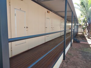 Una hilera de habitaciones blancas con puertas, una terraza de madera y una barandilla azul.