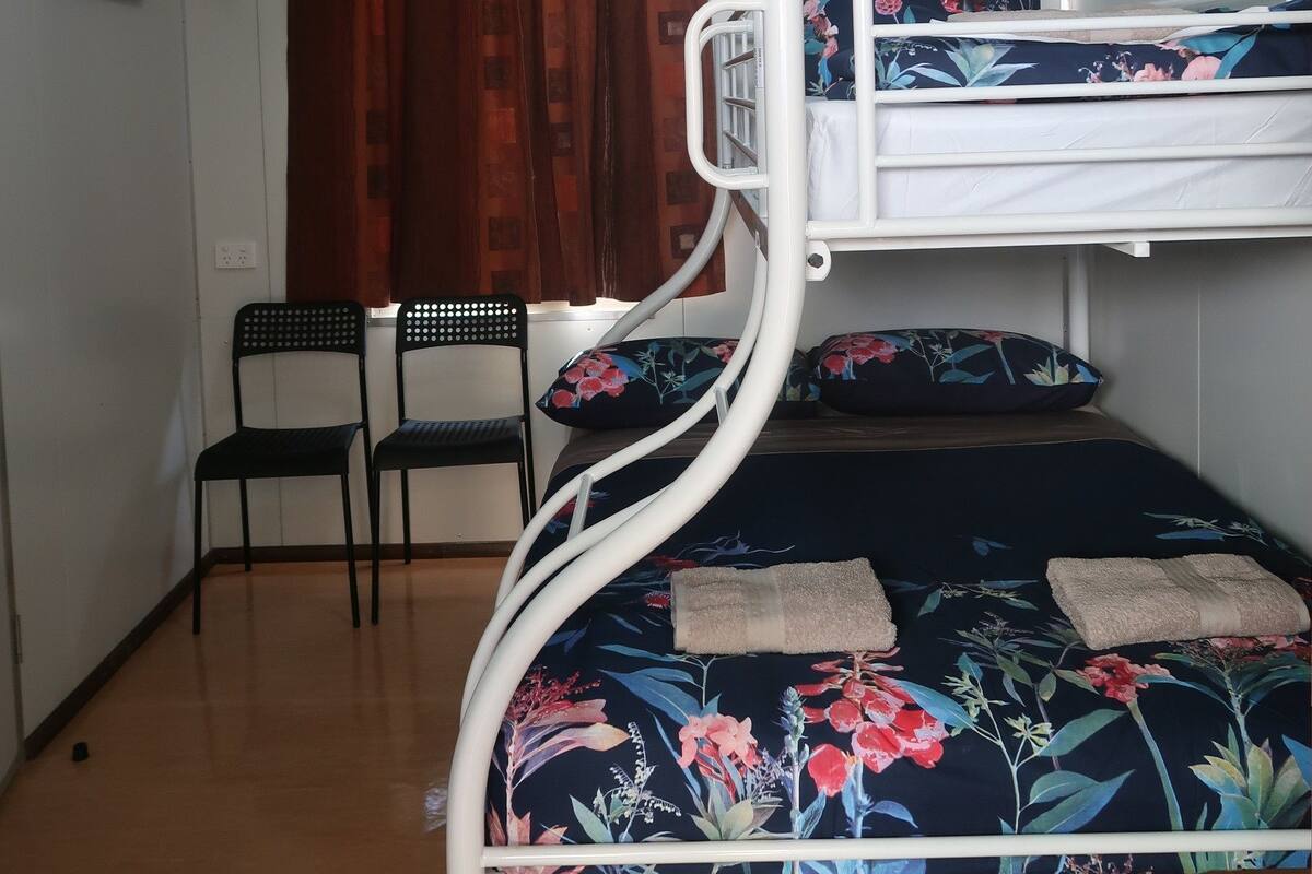 A bunk bed with floral bedding, a desk, two chairs, and a window with curtains.