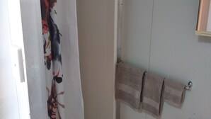 A bathroom with a shower curtain, a towel rack with towels, and a mirror on the wall. - Mud Crab Motel (Derby)