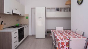 A compact kitchen with a built-in stove, a refrigerator, and a dining area with a table. - M200 - Marcelli, new two-room apartment 200mt from the sea (Marcelli)