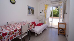 A small, well-lit room with a bed, a table with a patterned tablecloth, a chair, a small cabinet, and a window with curtains. - M200 - Marcelli, new two-room apartment 200mt from the sea (Marcelli)