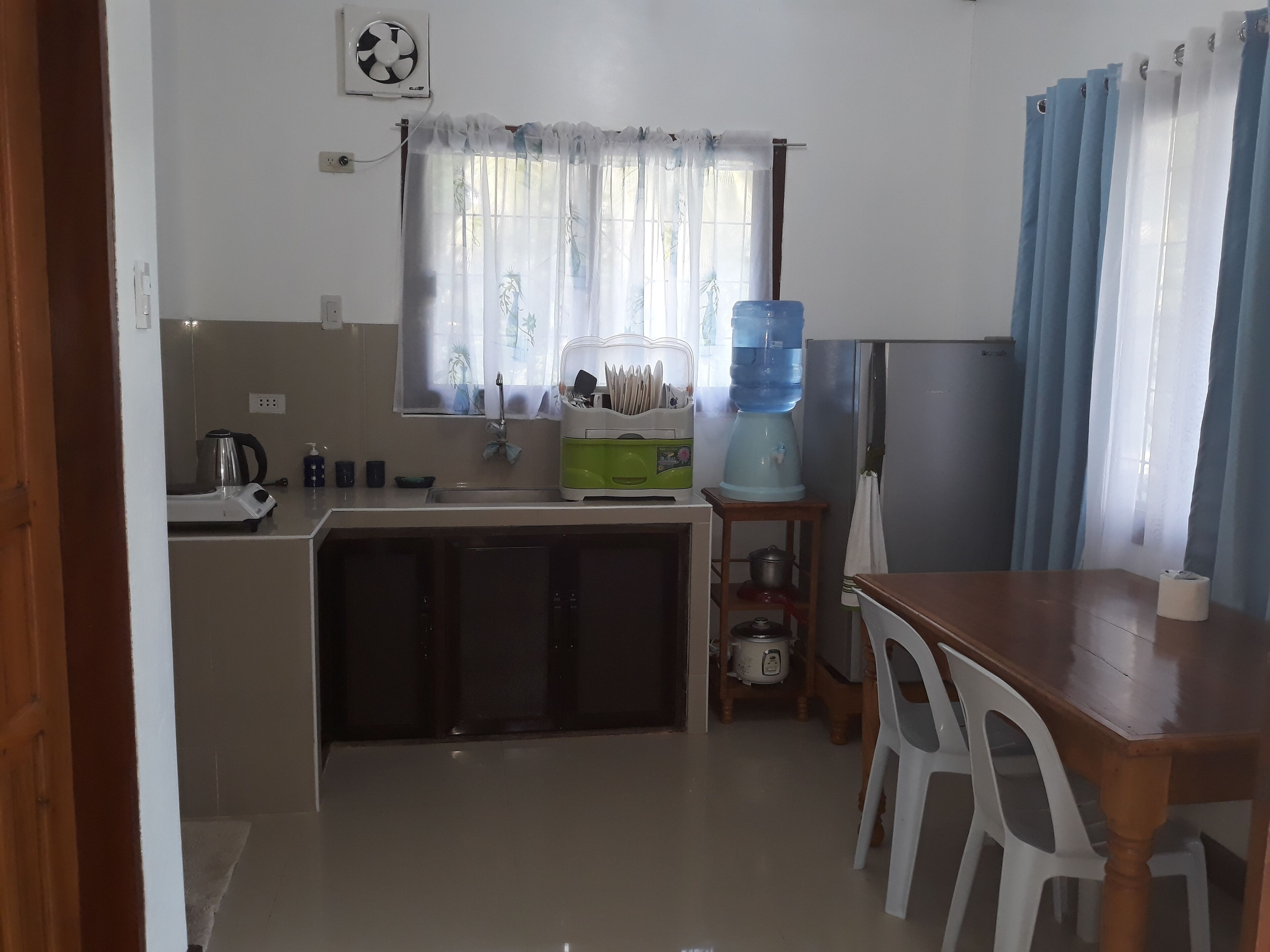 A compact kitchen with a sink, a kettle, a water dispenser, and a dining table with chairs.