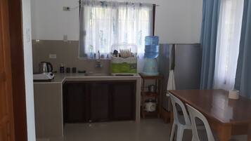 Cocina compacta con lavamanos, hervidor, dispensador de agua y una mesa de comedor con sillas.