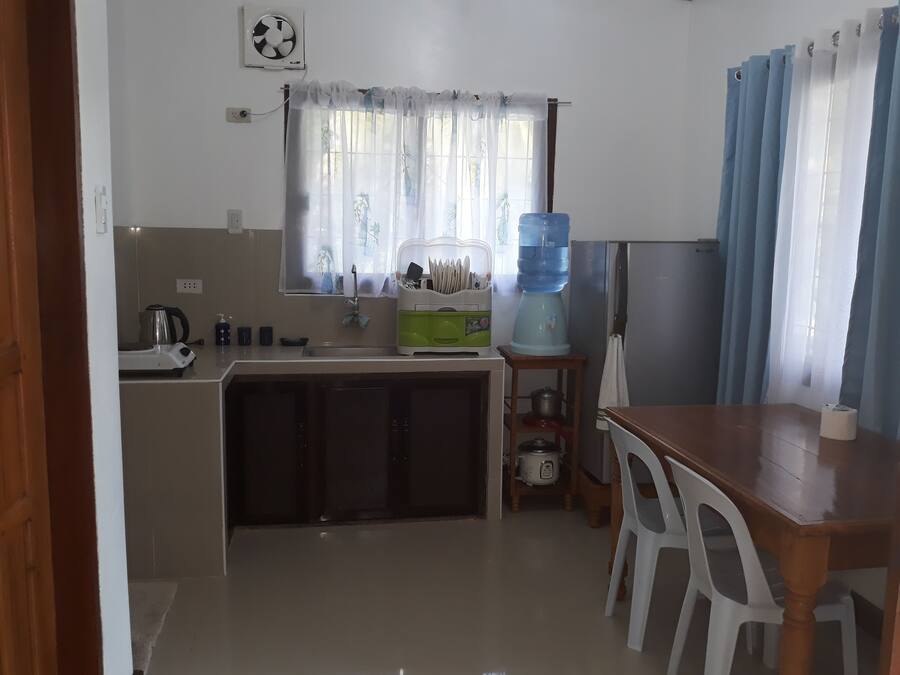Cocina compacta con lavamanos, hervidor, dispensador de agua y una mesa de comedor con sillas.